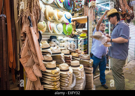 Venditore di raggiungere per mettere un cappello di paglia su un cliente shopping in un mercato di Oaxaca Messico Foto Stock