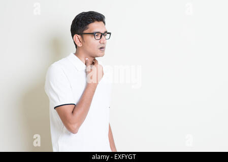 Ritratto di ragazzo indiano mal di gola, la mano sul collo della gola di compensazione. Uomo asiatico in piedi su sfondo semplice con ombra e copiare sp Foto Stock