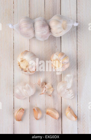 Vista aerea di aglio su un rustico tavolo bianco. Tre lampadine in una borsa a rete, due lampadine al di sotto del sacchetto, sparsi pezzi di pelle Foto Stock