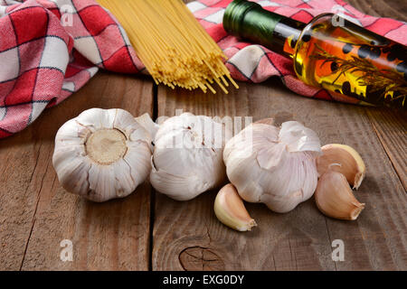 La cucina italiana ancora in vita su una tavola in legno rustico. 4 spicchi di aglio in primo piano con olio di oliva spaghetti secchi e rosso e wh Foto Stock