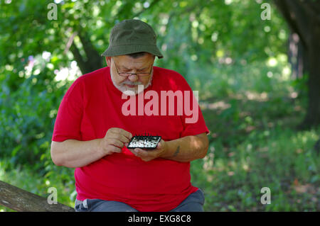 Senior uomo barbuto riproduzione di mini-scacchi con se stesso in un parco Foto Stock