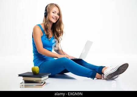 Felice giovane ragazza seduta sul pavimento con laptop e ascoltare la musica nelle cuffie. Guardando la fotocamera Foto Stock