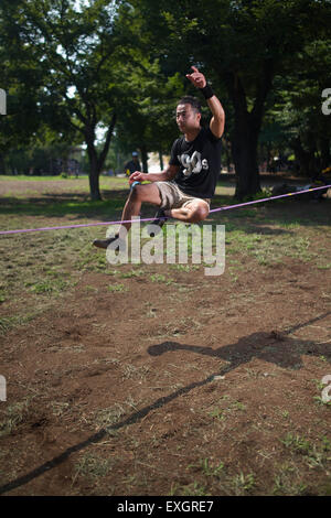 Un uomo giapponese in equilibrio su una slackline in un parco di Tokyo Foto Stock