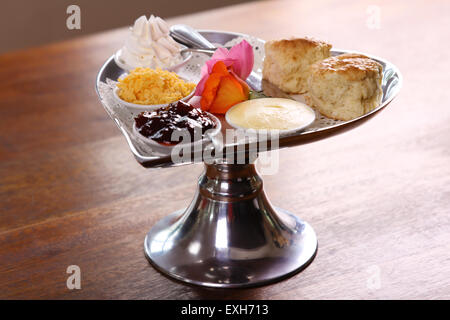 Burro di deliziosi scones su un cuore di argento vassoio sagomato servito con rose crema al formaggio e marmellata conserva su di un tavolo di legno. Foto Stock