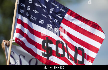 WAUKESHA, WI/STATI UNITI D'America - 13 Luglio 2015: un uomo detiene un flag che protestavano gli investimenti aziendali in American elezioni politiche di fronte all'Waukesha Convention Center di Waukesha, Wisconsin durante una progressiva protesta politica. Foto Stock