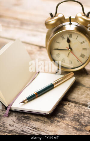 Aprire il notebook di piccole dimensioni con retro stile penna di fontana e sveglia dietro. La scrittura di sfondo vintage Foto Stock