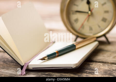 Aprire piccolo taccuino con penna stilografica e vecchia sveglia dietro. La scrittura di immagine di sfondo con il fuoco selettivo Foto Stock