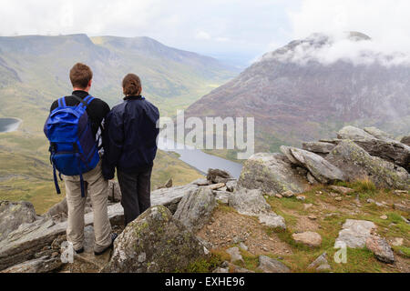 Giovane maschio e femmina escursionisti guardando giù verso Llyn Ogwen lago dal monte Tryfan con basse nubi in Snowdonia Wales UK Foto Stock