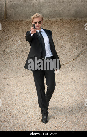 Uomo che cammina verso qualcuno puntando una pistola , pronti a sparare indossando un abito nero. Foto Stock