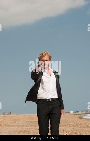 L'uomo puntando una pistola verso la telecamera , che mira a sparare indossando un abito nero. Foto Stock