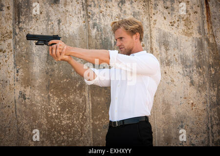 Uomo in camicia bianca puntando una pistola per sparare qualcuno. Foto Stock