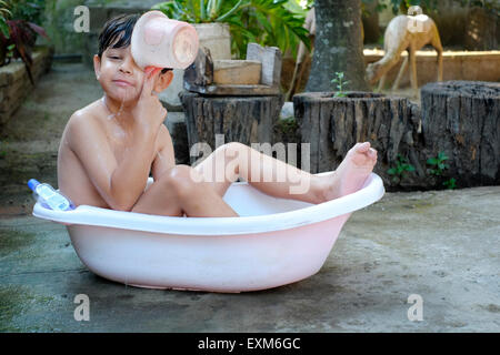 Little Boy di balneazione in un recipiente di plastica nel giardino anteriore in java indonesia Foto Stock