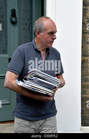L'uomo alla sua porta holding pila di cataloghi che egli è tenuto al contenitore di riciclaggio, Holloway, London Borough di Islington REGNO UNITO Foto Stock