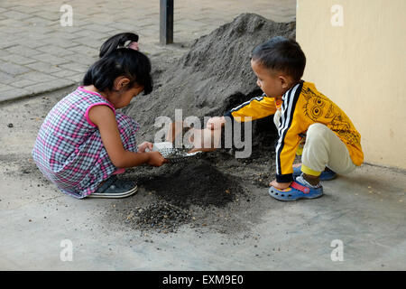 Bambini che giocano in una pila di sabbia nera essendo utilizzato per costruire una casa di estensione in un villaggio in java indonesia Foto Stock