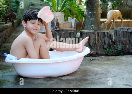 Little Boy di balneazione in un recipiente di plastica nel giardino anteriore in java indonesia Foto Stock