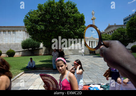 Università di Atene / Panepistimiou street zona specchiata sul vetro di una specchio trattenuto dai migranti africani street venditore. Atene Foto Stock