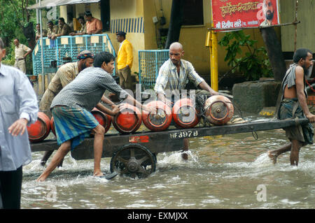 Lavoratori portano il GPL bombole di gas dal lato della spesa in allagato acqua causati a causa di forte pioggia a Bombay Mumbai; Maharashtra, India Foto Stock