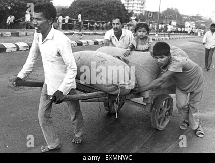 Gli uomini di spinta handcart caricati sacchi gunny sacchi bambino Mumbai India Foto Stock