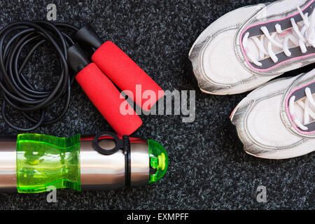 Sneakers, saltando la corda e bottiglia di acqua su uno sfondo scuro Foto Stock