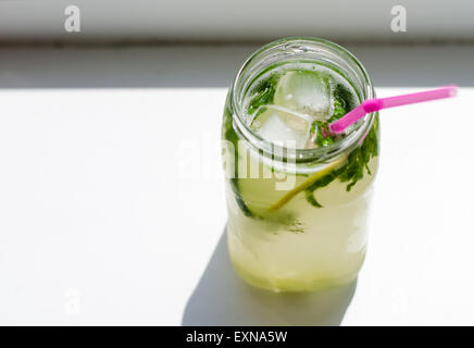 Un vetro ( un vaso ) di limonata a freddo con basilico, fette di cetriolo, cubetti di ghiaccio e paglia rosa Foto Stock