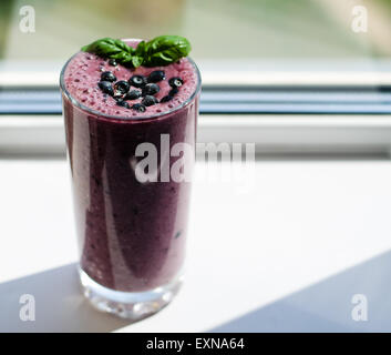 Un bicchiere di mirtillo - banana smoothie decorate con mirtilli freschi e basilico foglie su un top Foto Stock