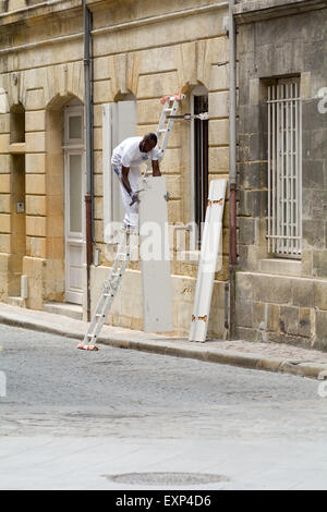 L uomo sulla scala la riparazione di persiane alle finestre al di fuori di casa a Bordeaux Francia Foto Stock