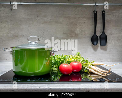 Smalto verde stewpot con prezzemolo e due pomodori nero sul fornello ad induzione Foto Stock