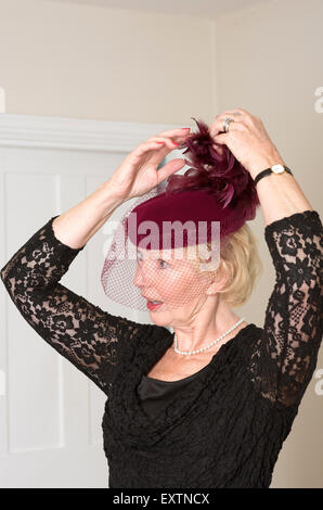 Donna anziana regolando il suo colore marrone cappello e il Velo con piume Foto Stock