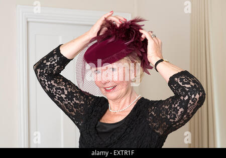 Donna anziana regolando il suo colore marrone cappello e il Velo con piume Foto Stock