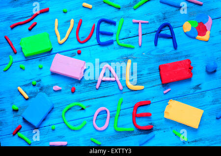 La frase vuelta al cole, torna a scuola in spagnolo, scritto con argilla di modellazione di diversi colori su un blu in legno rustico Foto Stock