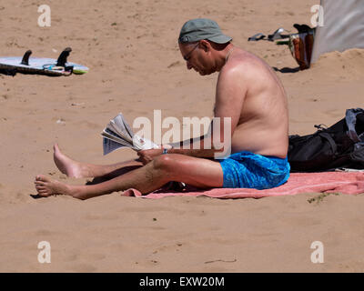 Uomo seduto sulla spiaggia leggendo un giornale, Woolacombe, Devon, Regno Unito Foto Stock