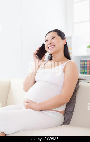 Donna incinta tenendo il telefono cellulare e sorridente felicemente, Foto Stock