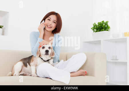 Giovane donna seduta con il cane e sul telefono, Foto Stock