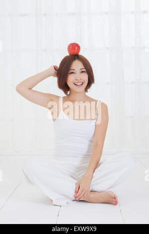 Giovane donna seduta sul pavimento con un Apple sulla testa, Foto Stock