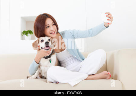 Giovane donna tenendo il telefono cellulare e abbracciando il suo cane, Foto Stock