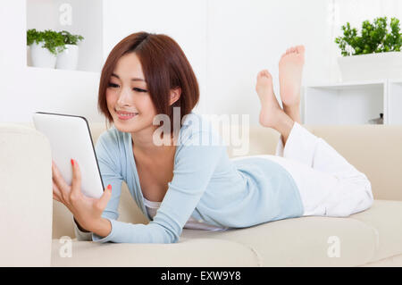 Giovane donna sdraiata sul divano e utilizzo degli appunti con sorriso, Foto Stock