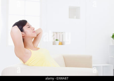 Giovane donna seduta su un divano con le mani dietro la testa, Foto Stock