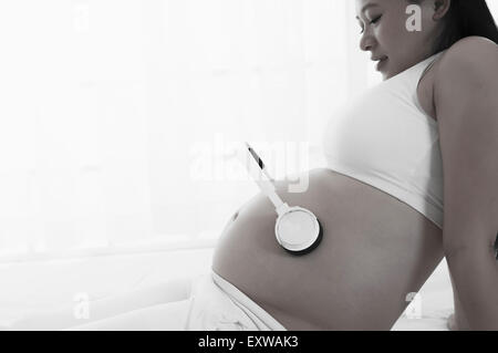 Donna incinta mettendo le cuffie sull'addome, Foto Stock