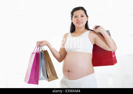 Donna incinta holding shopping bags e sorridente alla telecamera, Foto Stock