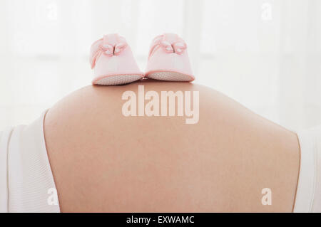 Un paio di scarpe per bambini su della donna incinta, addome, Foto Stock