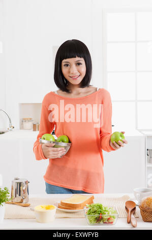 Giovane donna azienda mele verdi e sorridente alla telecamera, Foto Stock