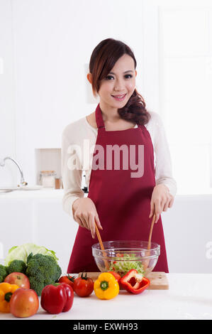 Giovane donna rendendo insalata con sorriso, Foto Stock