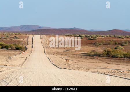 Ampia, dritta strada di ghiaia nel paesaggio secco, Regione di Kunene, Namibia Foto Stock