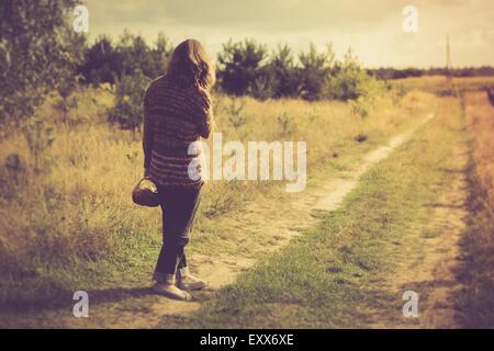 Ragazza in un maglione a piedi da rurale strada erbosa nel paesaggio di campagna. Foto con umore vintage Foto Stock