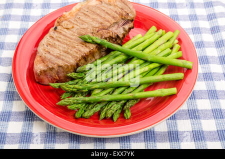 Nastro grigliato bistecca su una targhetta rossa con asparagi Foto Stock