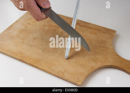 L'uomo affila il coltello con affilatrice sul tagliere di legno Foto Stock