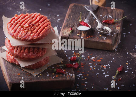 Materie di macinato di manzo hamburger di carne costolette di manzo con il condimento su vintage di tavole di legno, sfondo nero Foto Stock