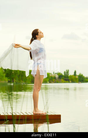 Donna con le braccia aperte in piedi alla fine del lago di pier Foto Stock