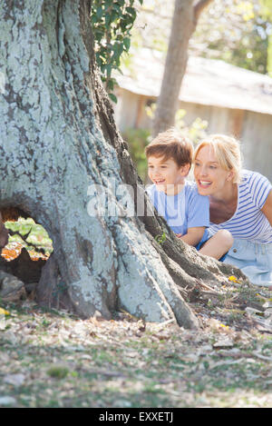 Ragazzo giovane e madre di nascondersi dietro tree, giocando a nascondino Foto Stock