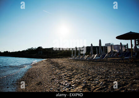 E sabbiosa spiaggia di ciottoli con sedie a sdraio e ombrelloni al tramonto Foto Stock